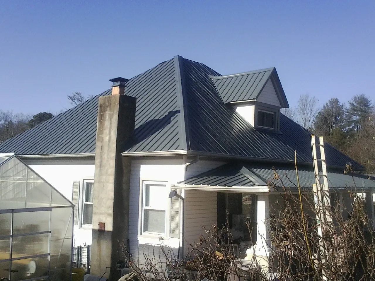 Dark blue standing seam metal roof on a white farmhouse with dormer — Slate & Tile Roof Repair by Roofing Brothers in Pine