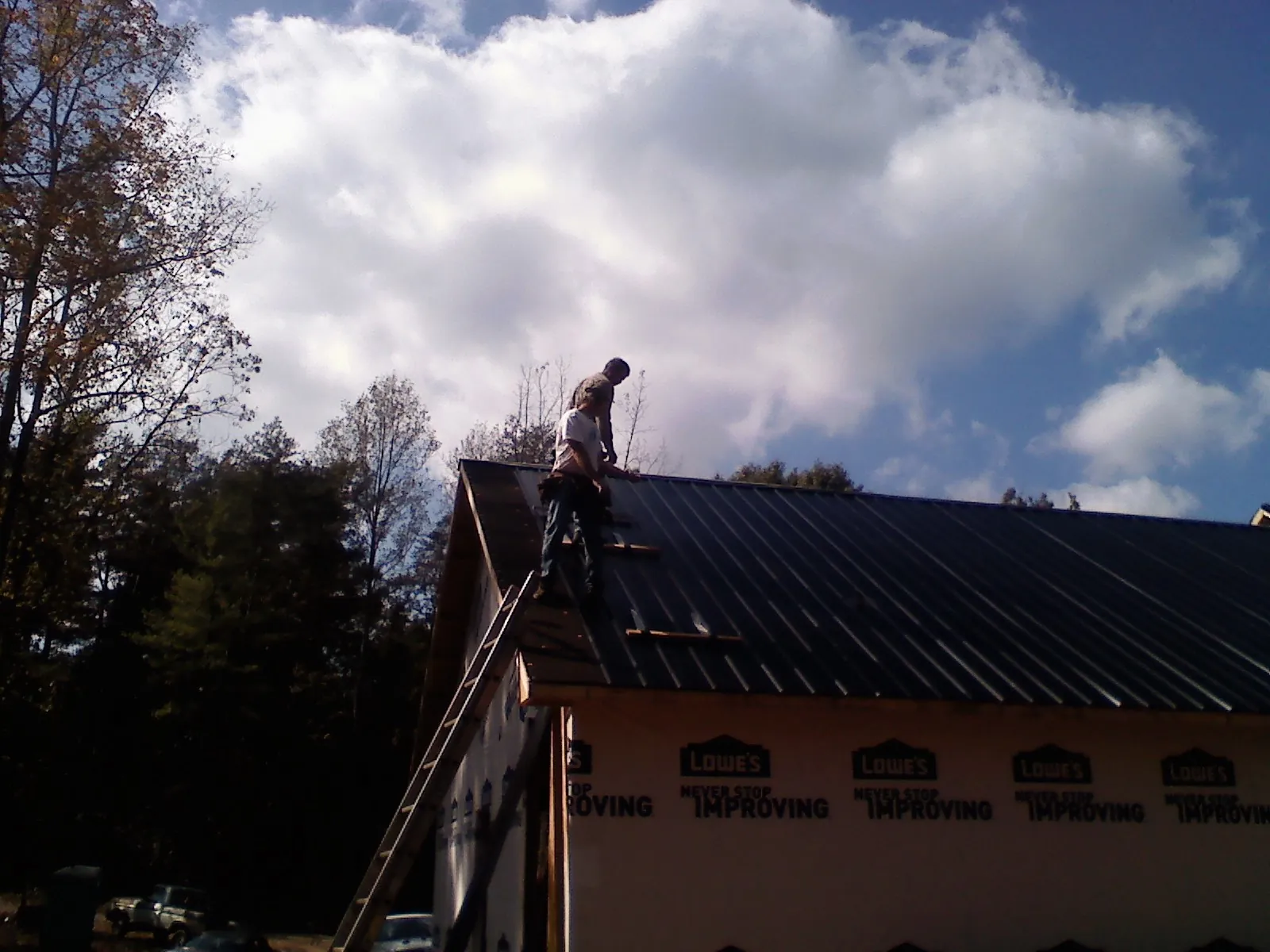 Roofer fastening dark metal panels high against a cloudy sky, from a Roof Inspection job in Pine