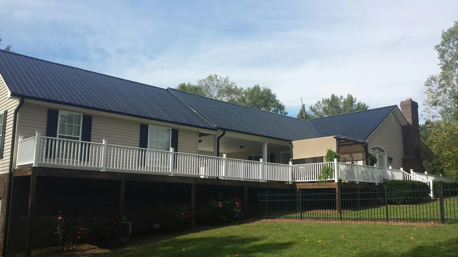Black metal roof above a long white railed deck on a hillside home in Pine
